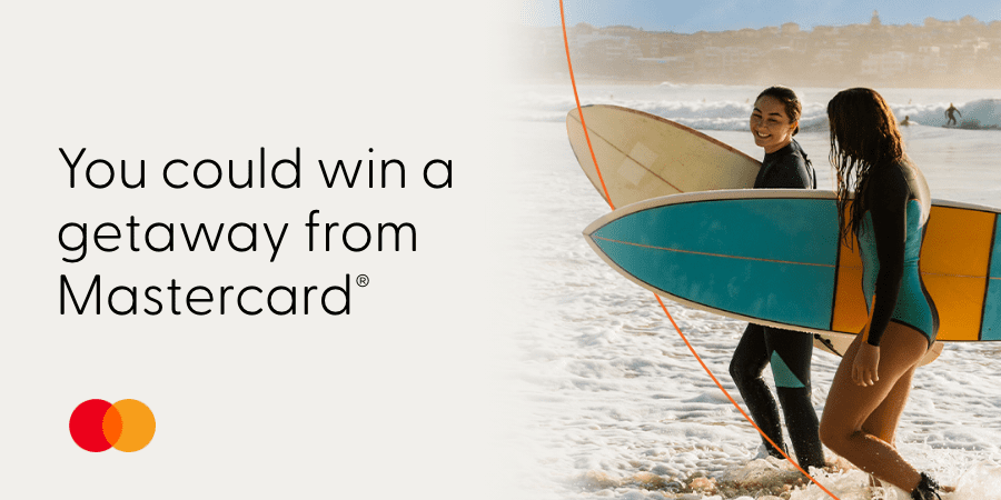 Two women surfers returning to shore. The words on the right: you could win a getaway from Mastercard&reg;