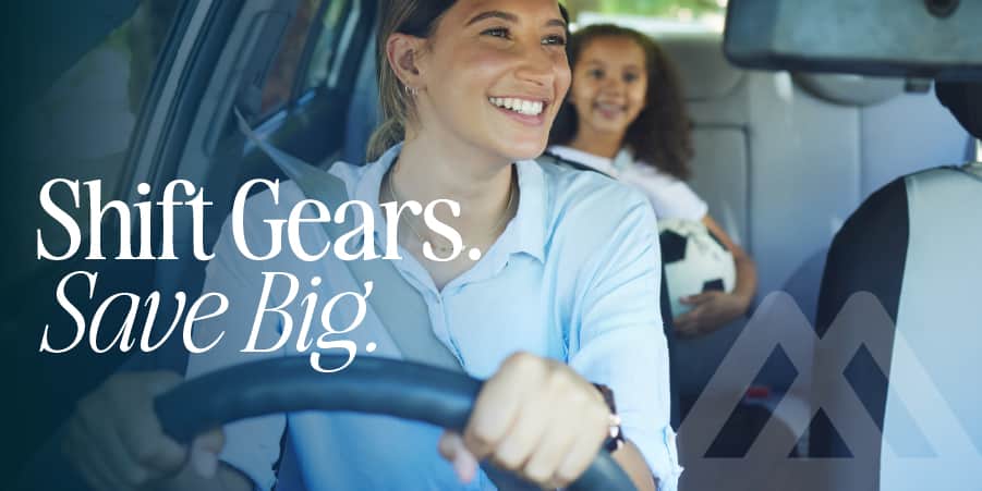 A smiling woman looking through her vehicle rear view mirror at her young daughter. At the left, the words: shift gears save big.