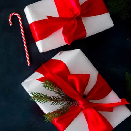 Two gifts wrapped with a red bow alongside a candy cane against a navy blue background.