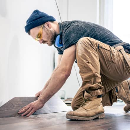 A construction worker laying hard wood floors inside a home.