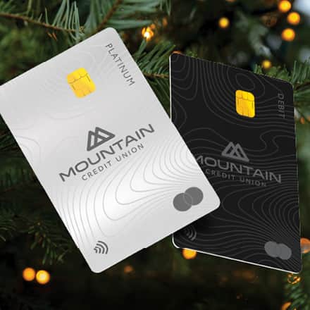The Mountain Credit Union credit and debit cards in front of Christmas tree branches.