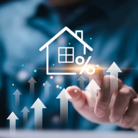 A hand with digital illustration of a house, percentage sign, and upward arrows representing rising mortgage or interest rates.