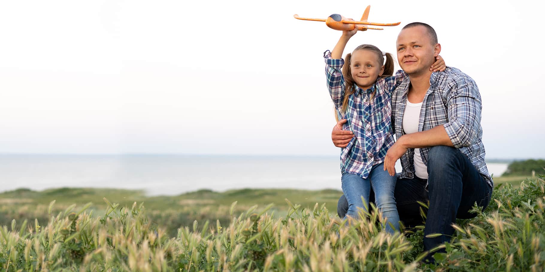 A father kneeling with his daughter helping her launch a toy plane.