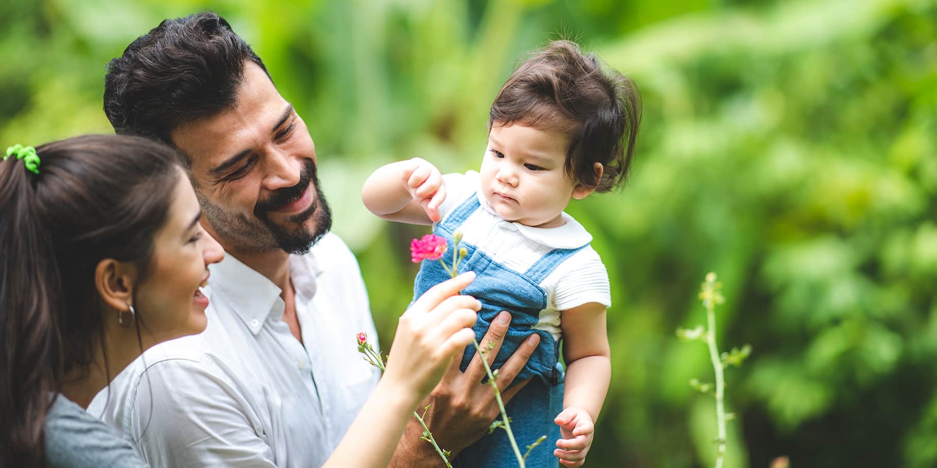 Two young parents carrying a baby in a flower garden.