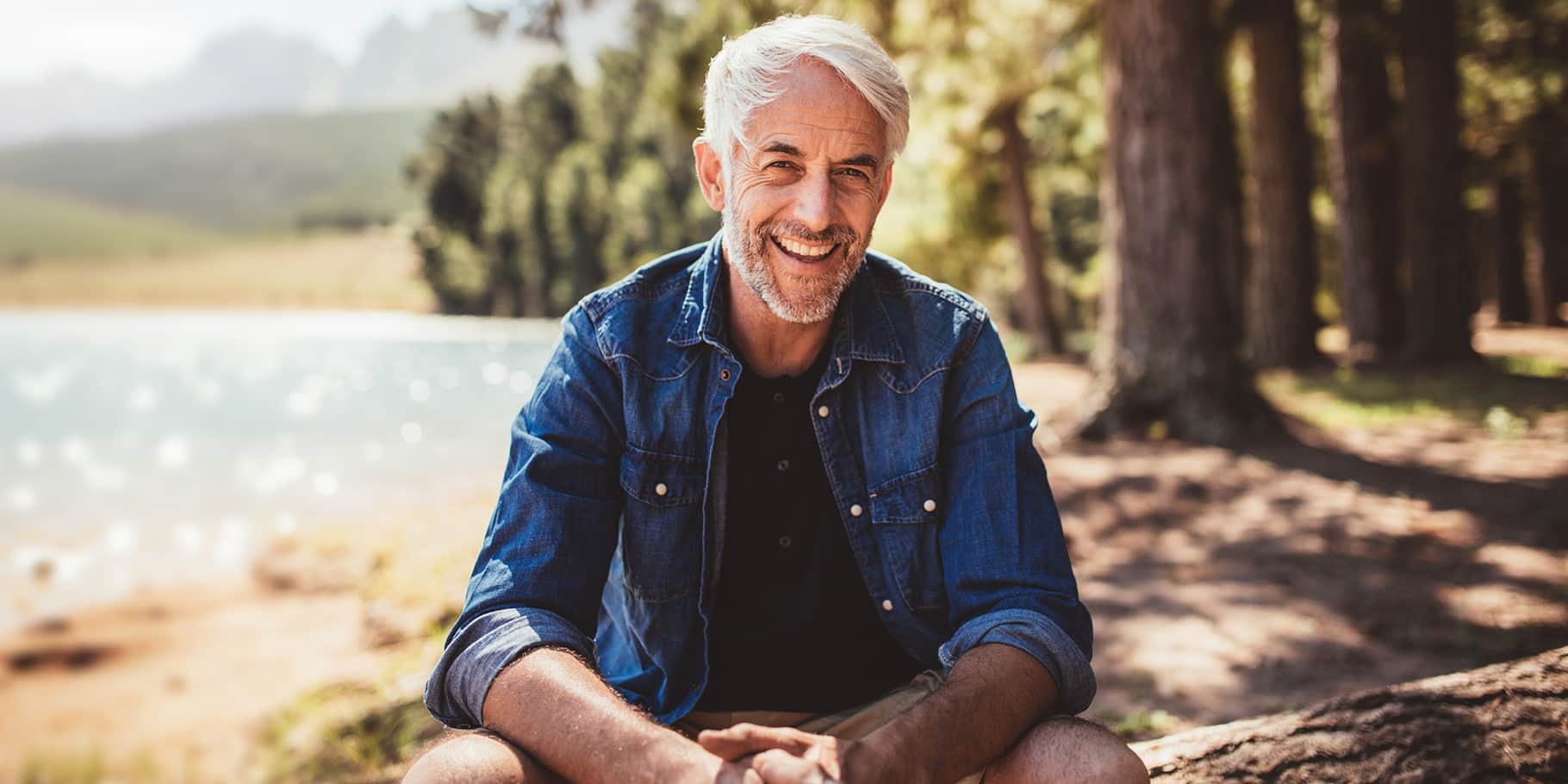 A elderly, happy and fit man kneeling down by the lakeside.