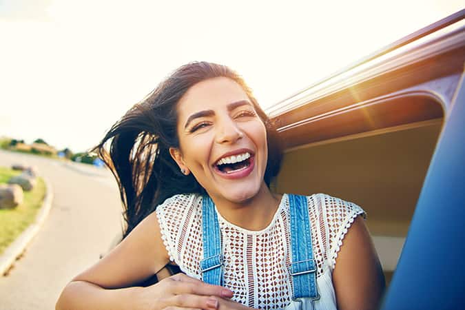 Smiling young woman sticking her head outside of a car window.