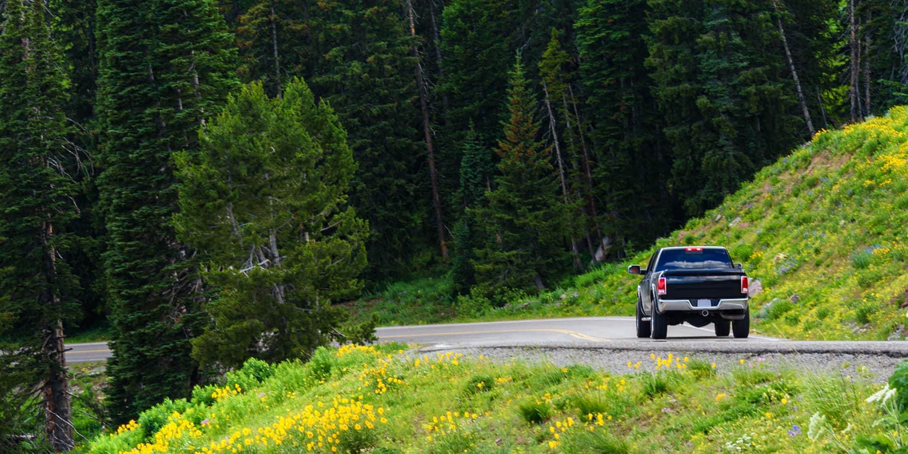 A black pickup truck driving along a mountainside winding road.