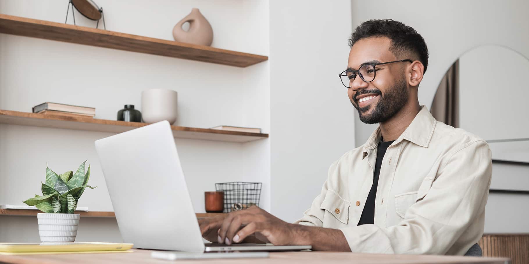 A smiling young man working on a laptop.