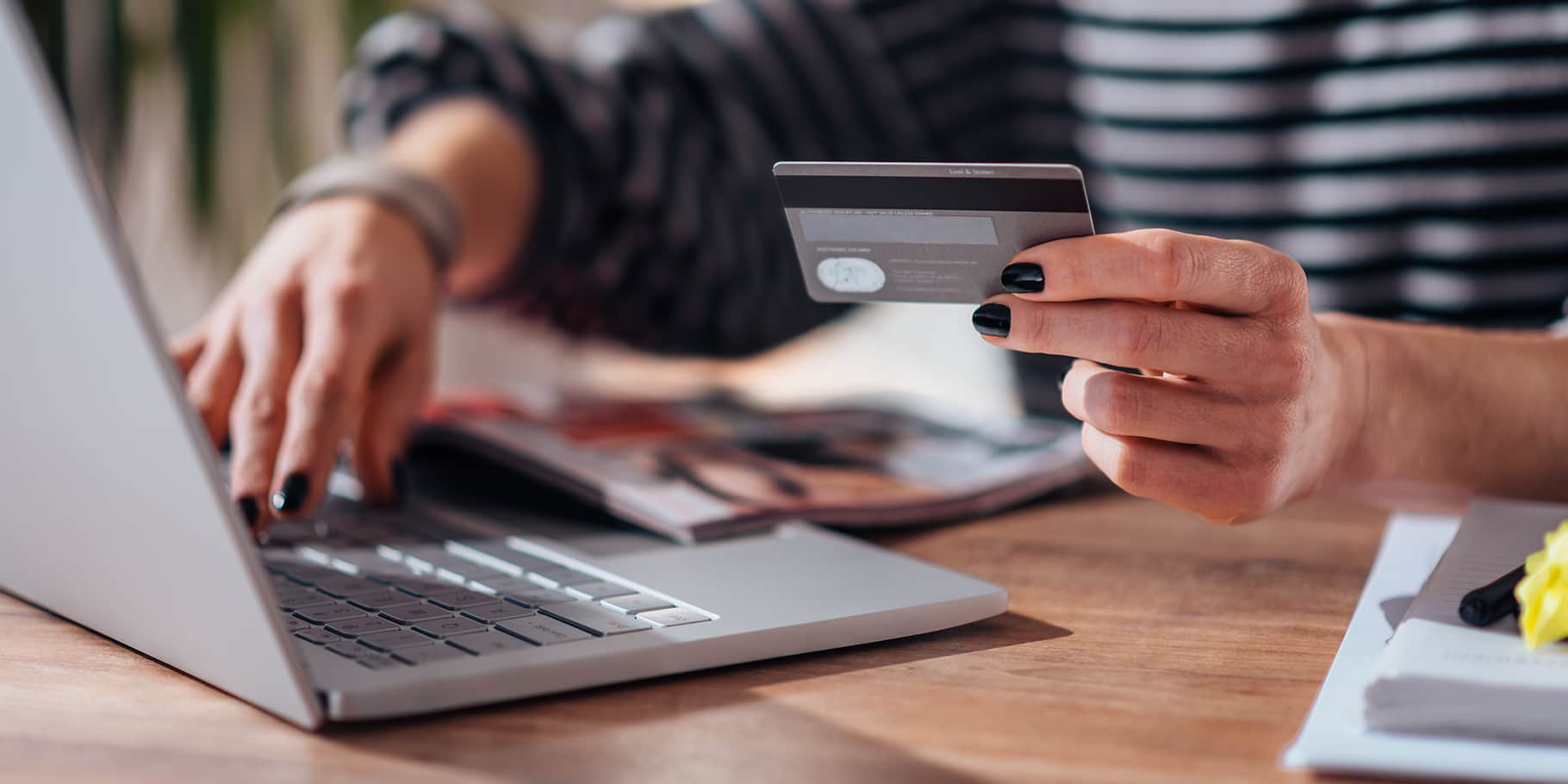 Female arms holding a credit card and typing on a laptop.