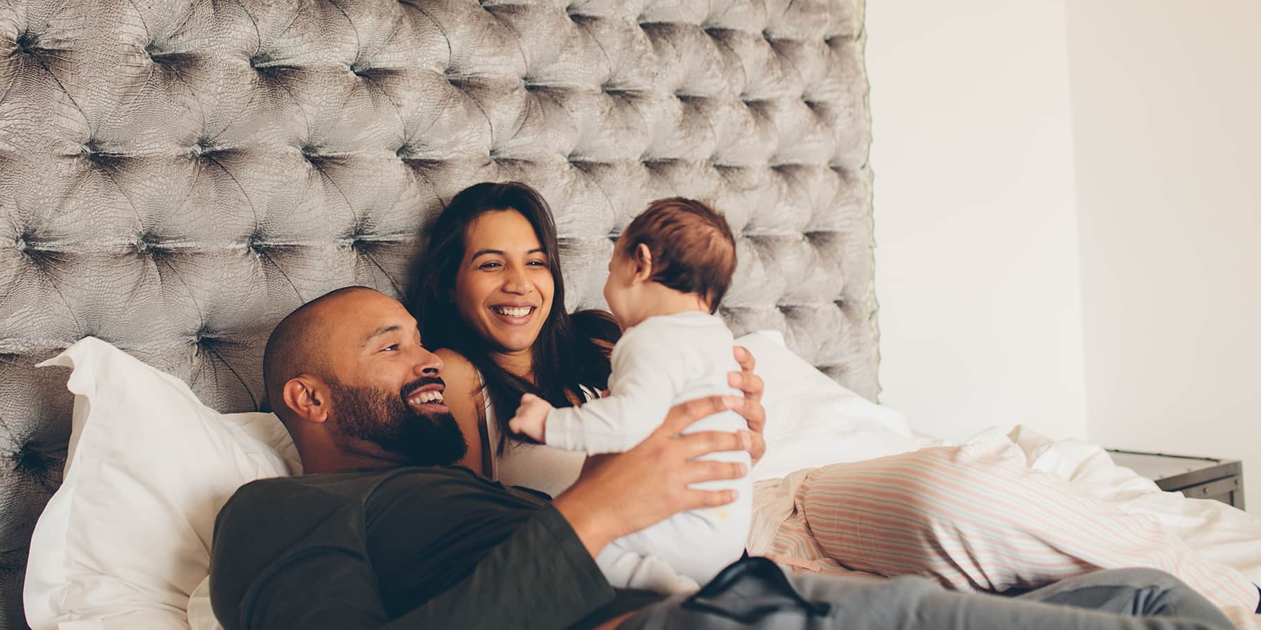A smiling father and mother with their baby on their bed.