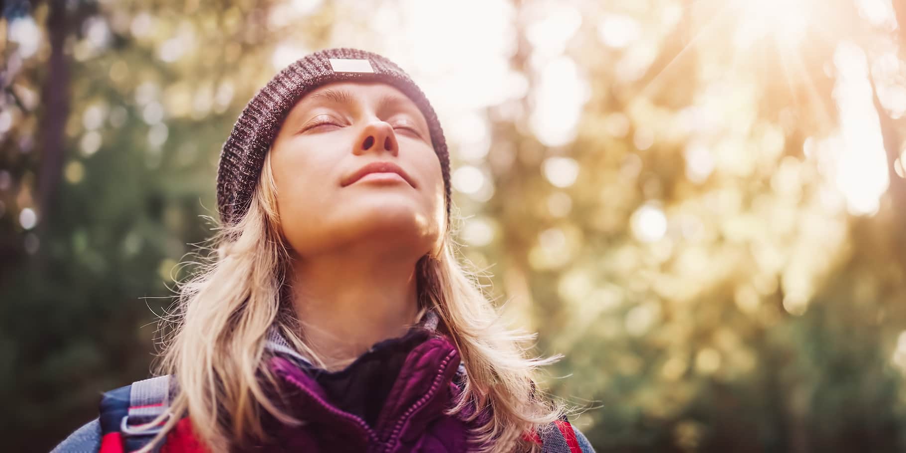 A smiling young woman out for a hike letting the sunshine hit her face.