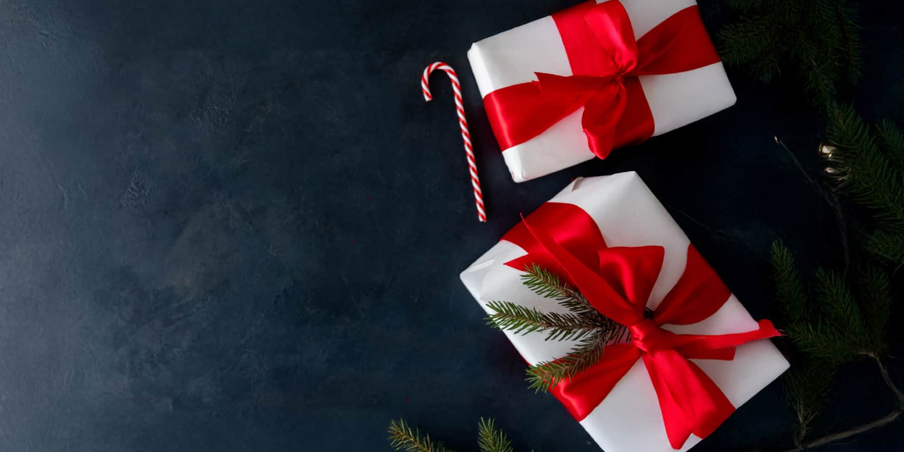 Two gifts wrapped with a red bow alongside a candy cane against a navy blue background.