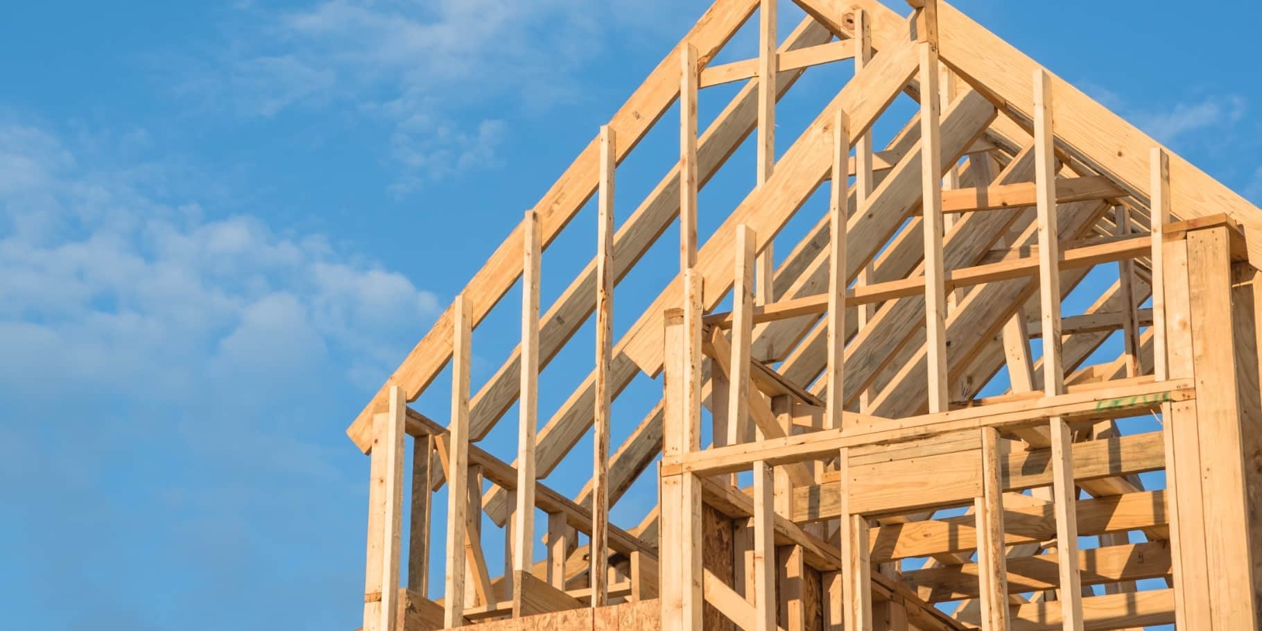 Wood framing of a new home under construction against a bright blue sky.
