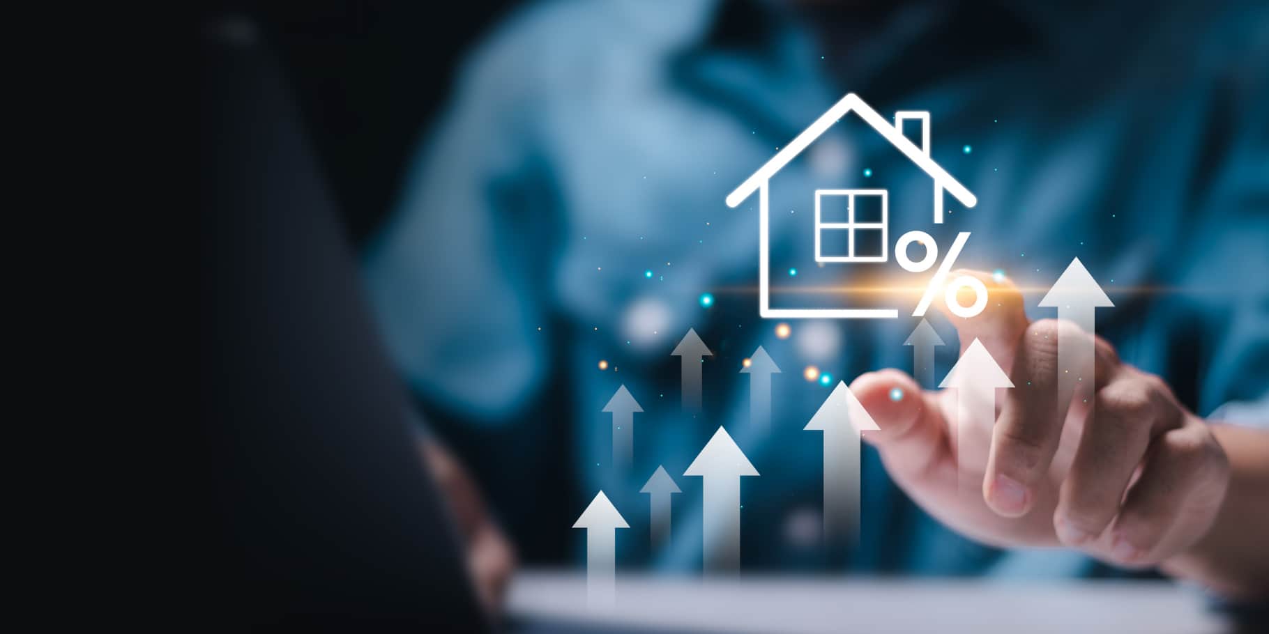 Person using a laptop with digital illustration of a house, percentage sign, and upward arrows representing rising mortgage or interest rates.