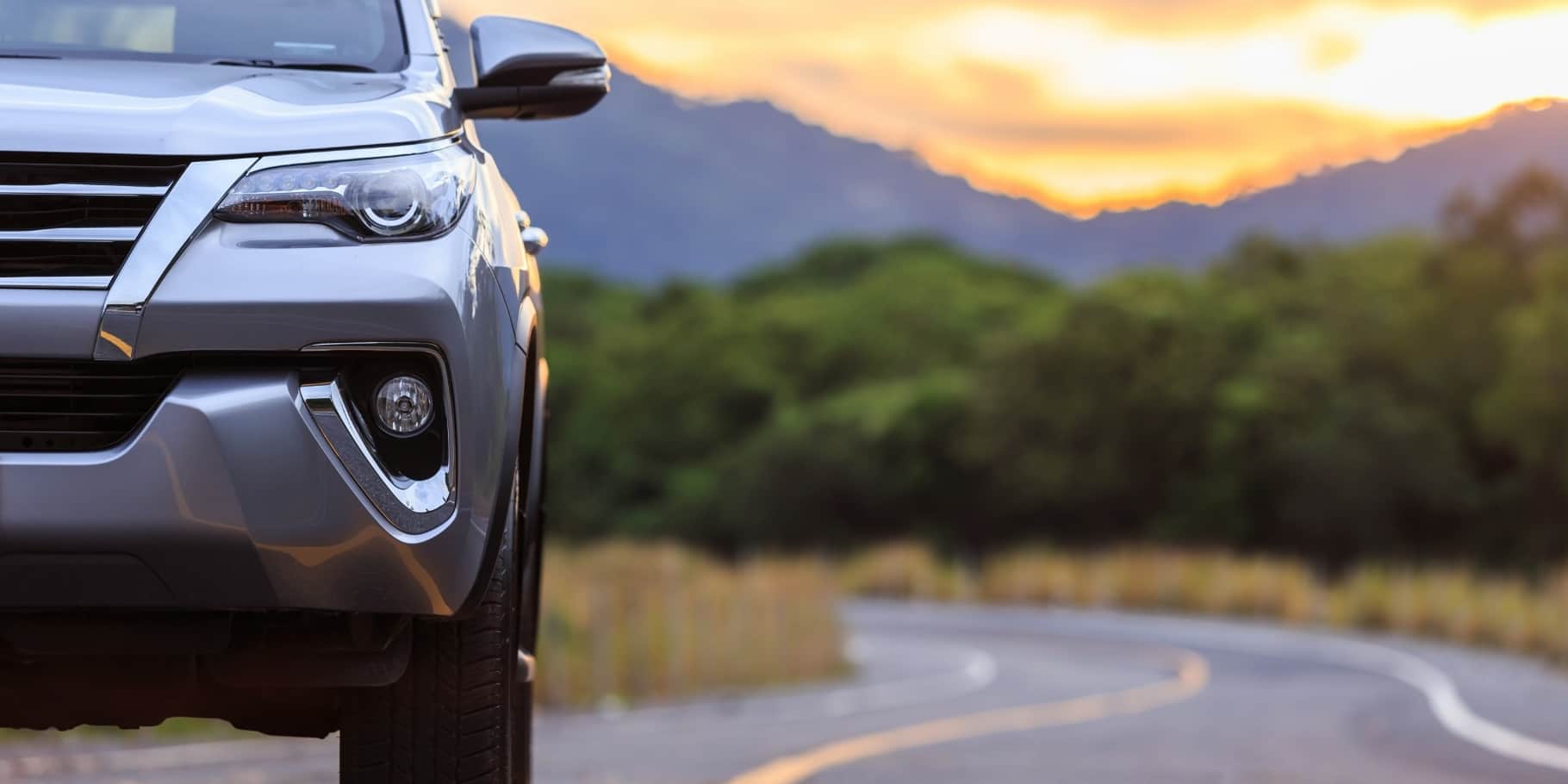 Front view of a silver SUV parked along a scenic mountain road at sunset.