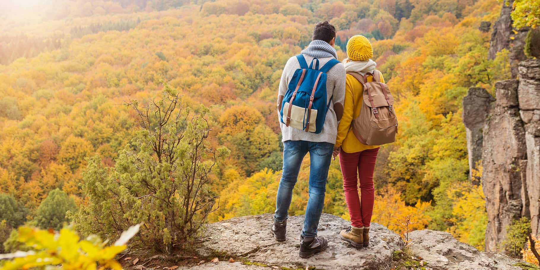 A young couple on a hike in fall overlooking the view from the top of a mountain.