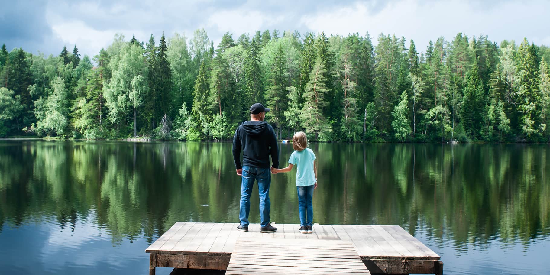 A father and his young child standing on a pier looking over a beautiful lake.